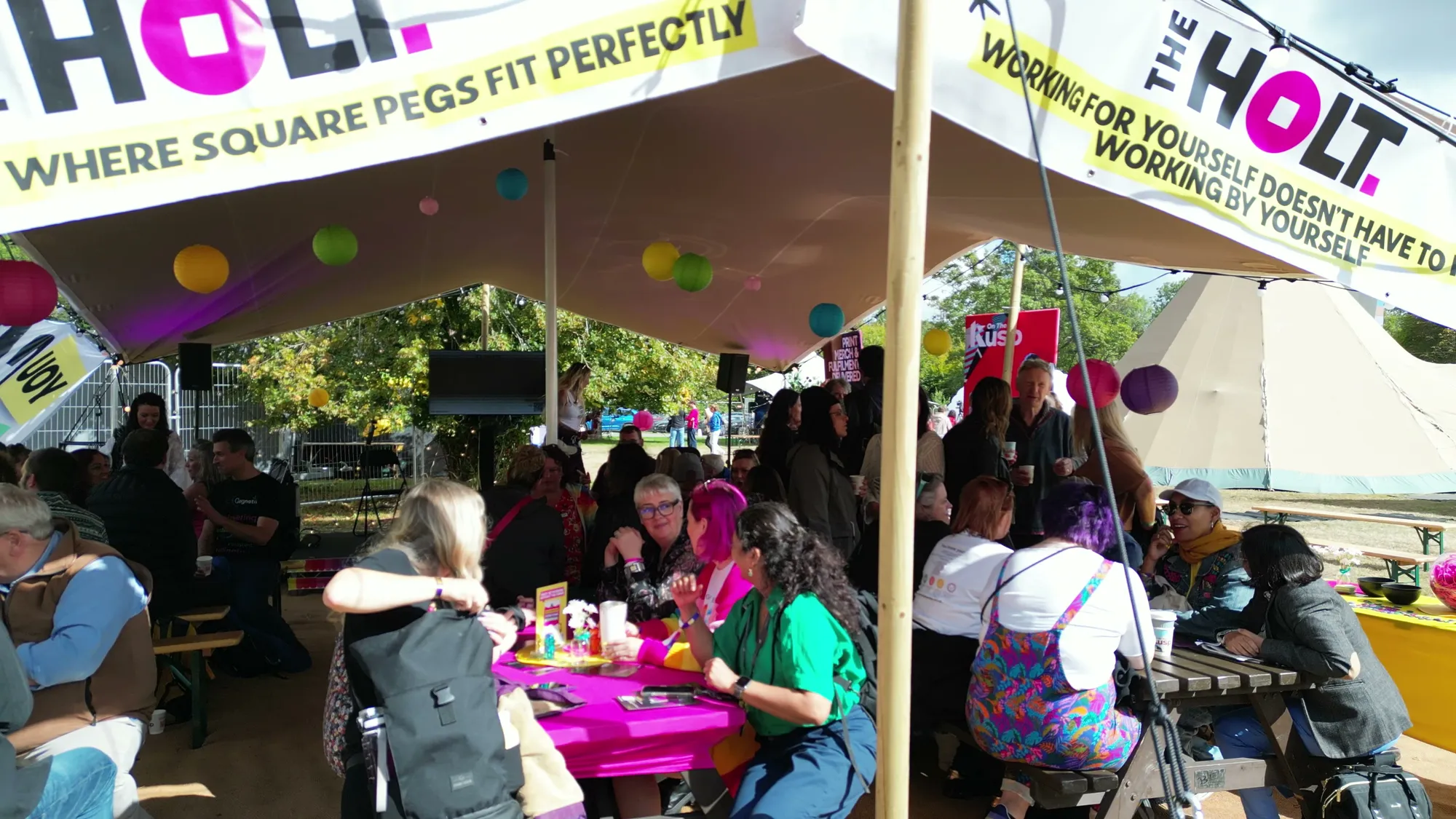 The HoLT tent at Ideas Fest 2026, packed with members round pink and yellow tables.